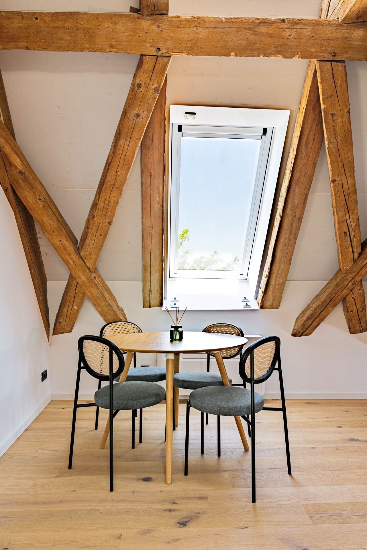 A dining area with a wooden table and chairs, a window with a view, and exposed wooden beams.