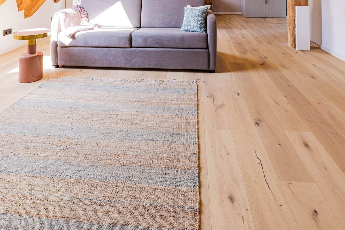 Une pièce de style loft avec des poutres apparentes, un canapé gris, un tapis tissé et une petite table ronde.