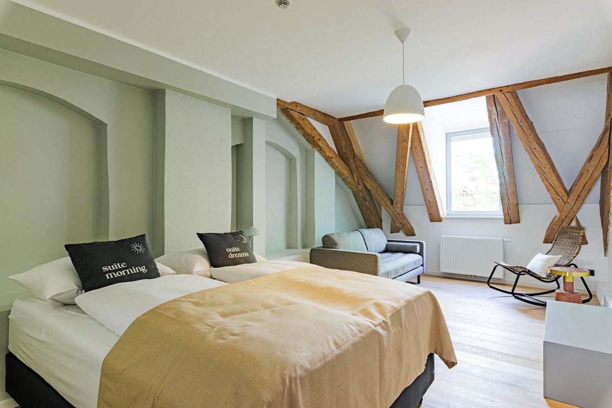 Une chambre avec deux lits, un luminaire suspendu, des poutres en bois et une fenêtre.