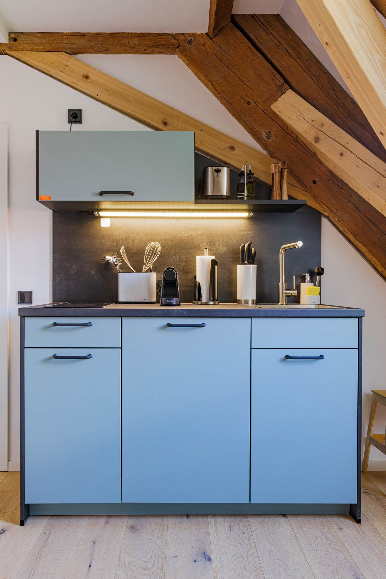A modern kitchen with blue cabinets, a stainless steel range hood, and a wooden ceiling.