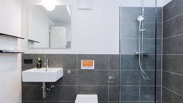Une salle de bain moderne avec un lavabo blanc, des toilettes et une douche à parois de verre.