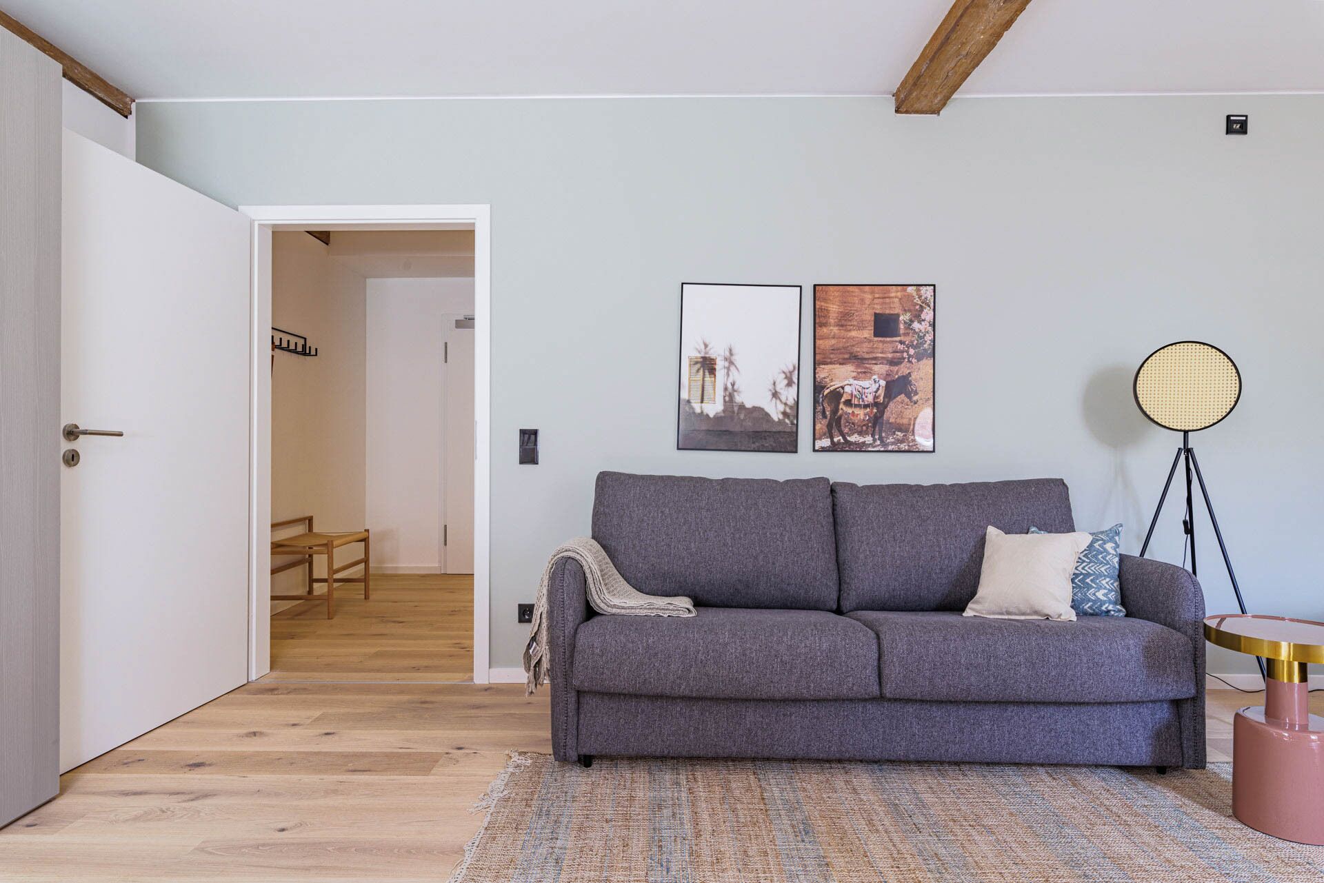 Una sala de estar con un sofá gris, un tapete estampado y dos cuadros en la pared.