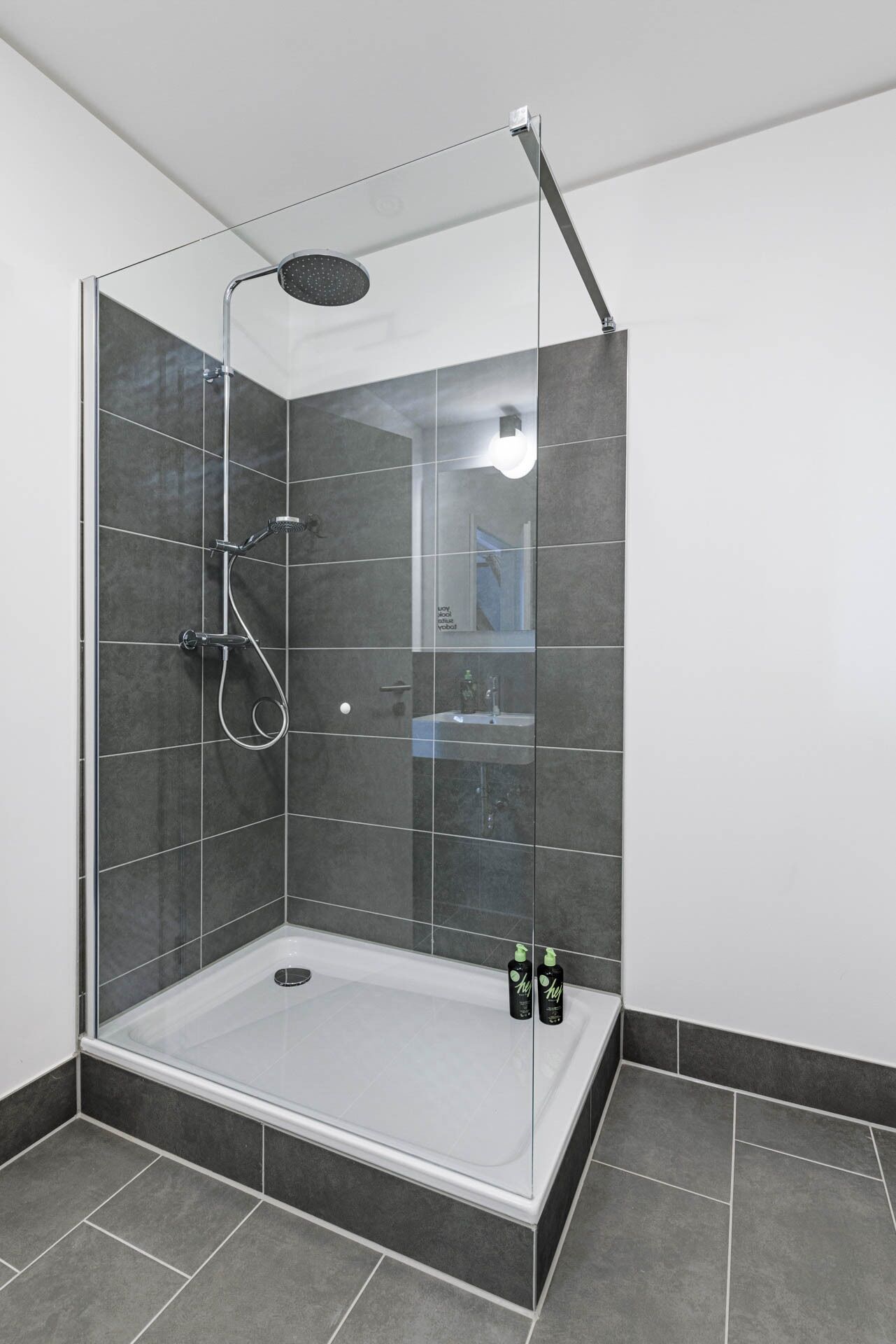 A modern shower enclosure with a glass door, a handheld showerhead, and a handheld shower head.