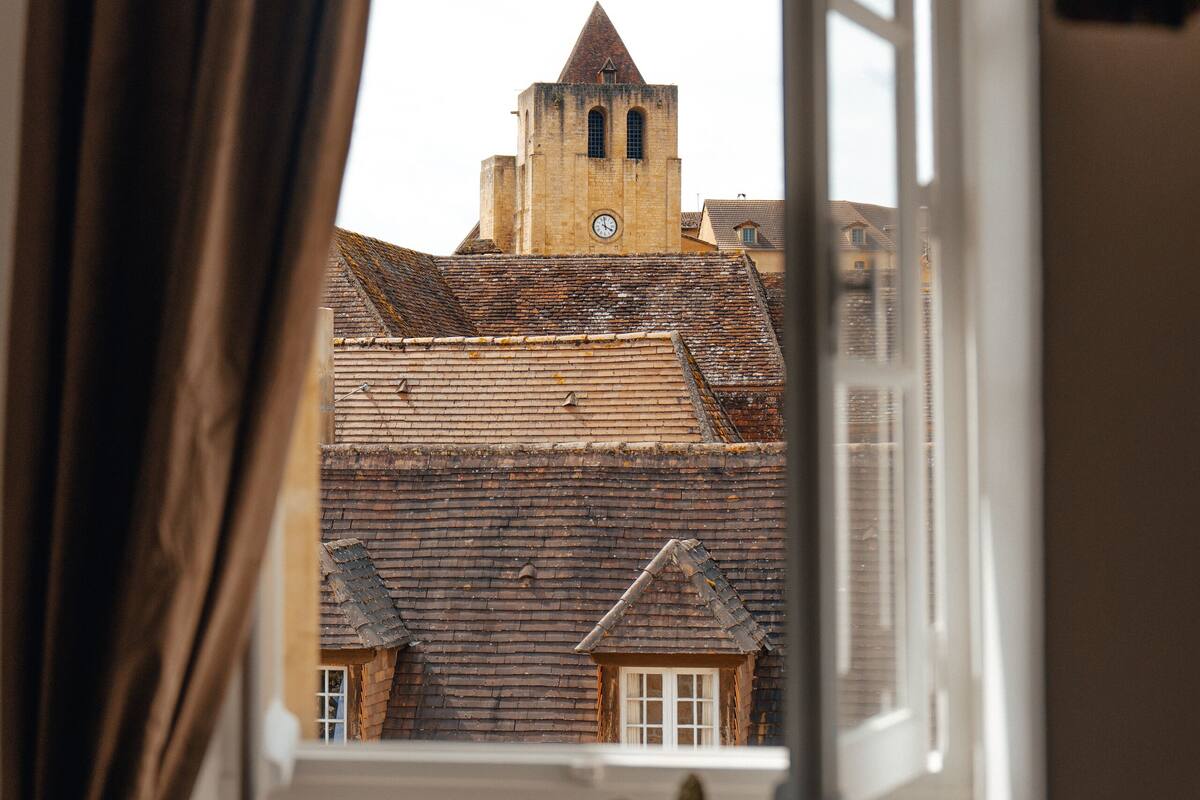 A view through an open window of a building with a clock tower, a wooden door, and a cactus plant.