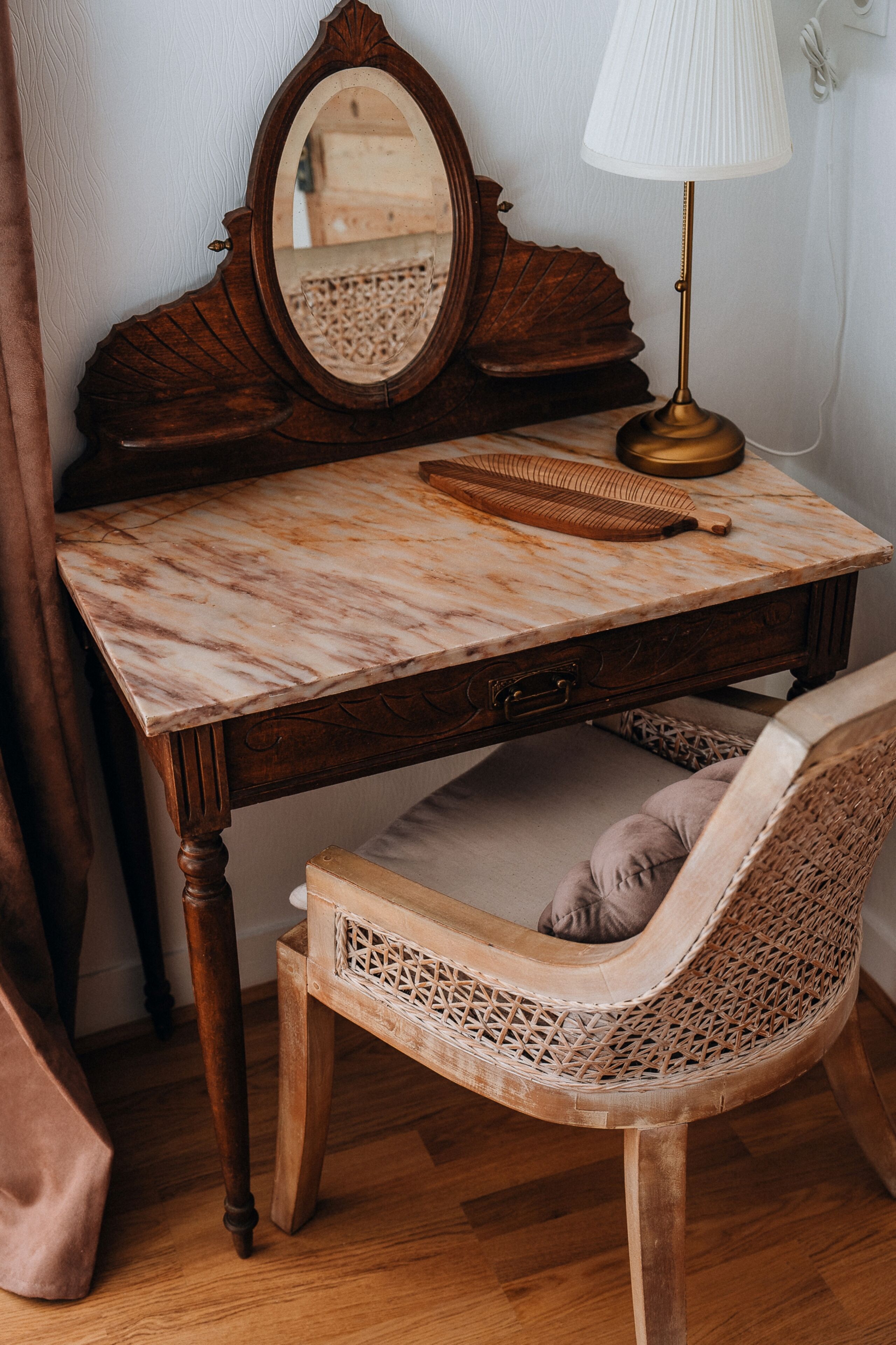 Un tocador de madera con encimera de mármol, un espejo, una lámpara y una silla de mimbre.