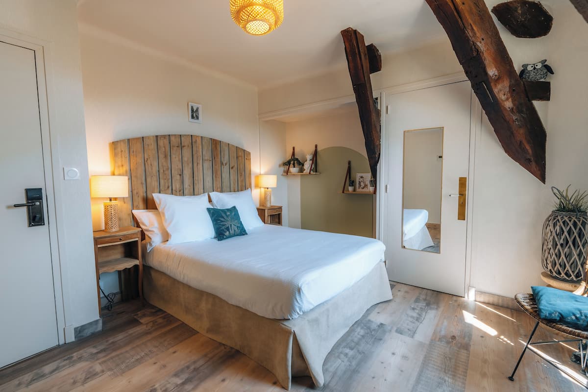 A bedroom with a large bed, wooden headboard, bedside lamps, a wooden floor, and a large mirror.