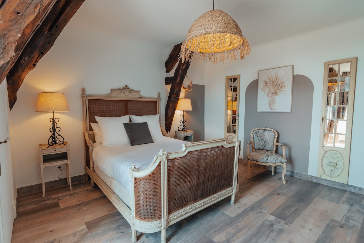 A bedroom with a large bed, two bedside tables with lamps, a chair, and a decorative mirror.