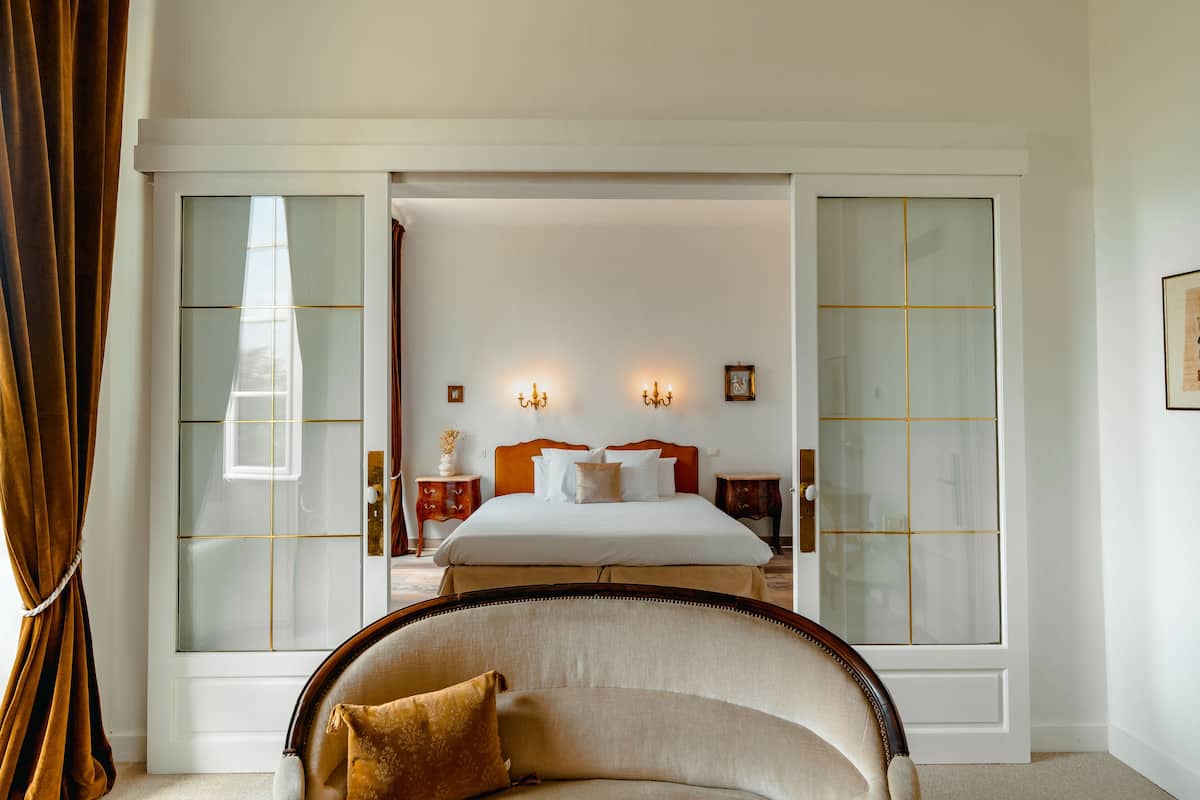 A hotel room with a large bed, two bedside tables, a chair, and a sliding glass door.
