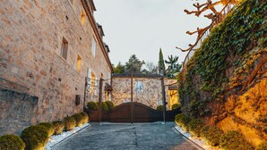 A stone building with a gated entrance, a paved pathway, and a row of bushes along the sides. - Hotel L'abbaye (Saint-Cyprien)