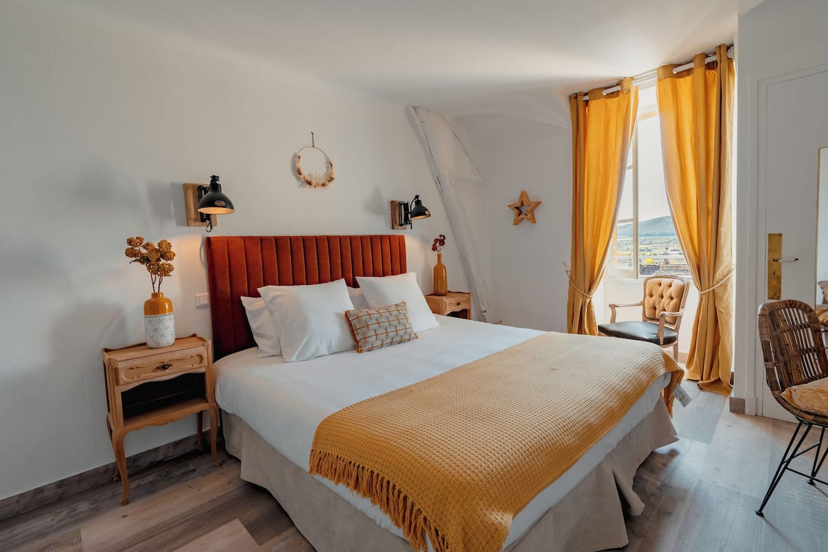 A neatly arranged hotel room with a large bed, a wooden nightstand, a chair, and a window with curtains.
