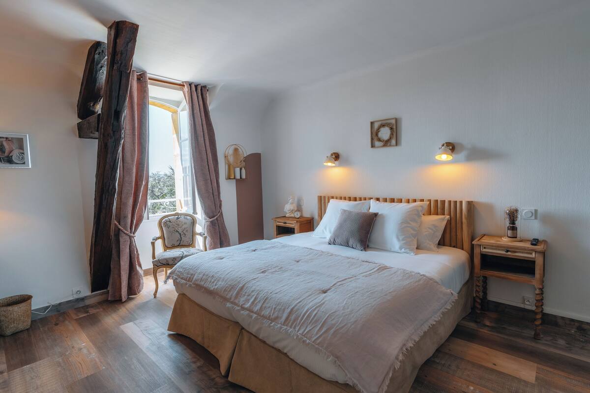 A bedroom with a large bed, wooden headboard, bedside tables, and a window with curtains.