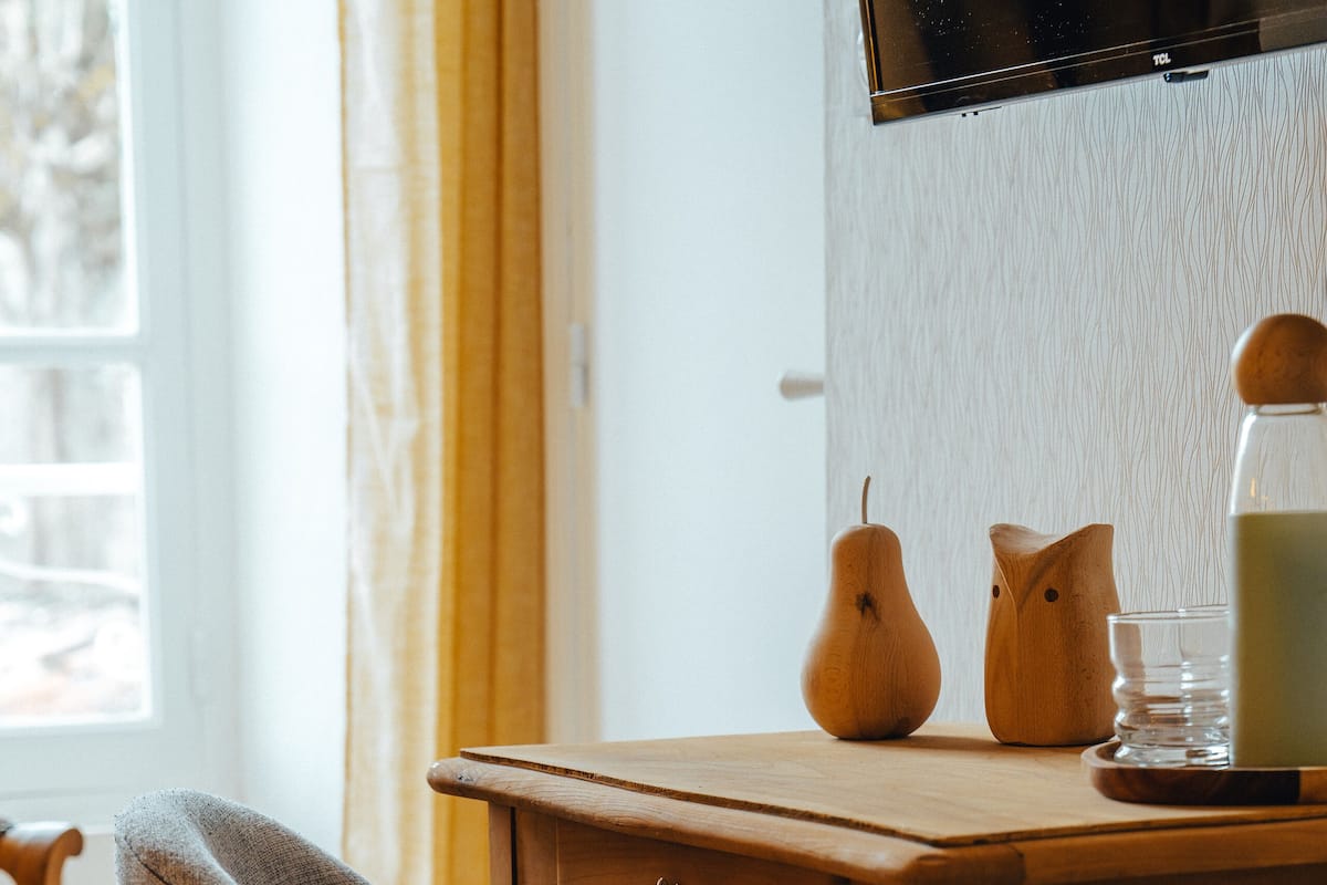 A wooden desk with a chair, a television mounted on the wall, and a window with curtains.