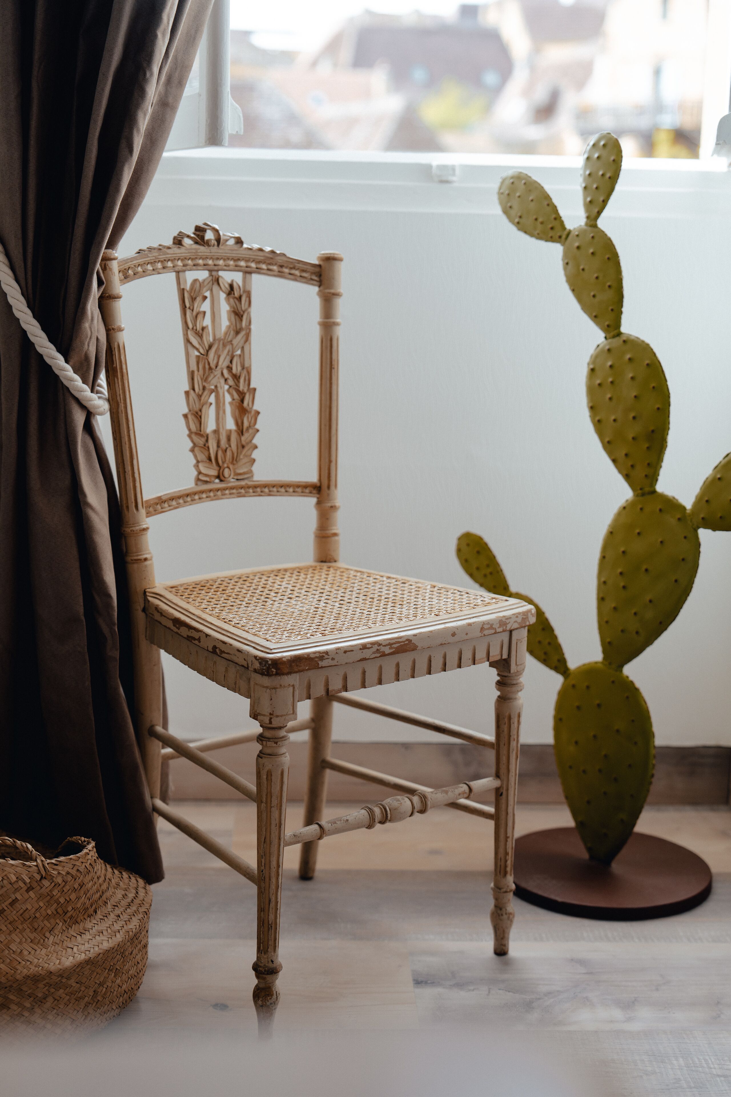 Une chaise en osier, avec un siège et un dossier tressés, placée à côté d’un grand cactus dans un pot rond.