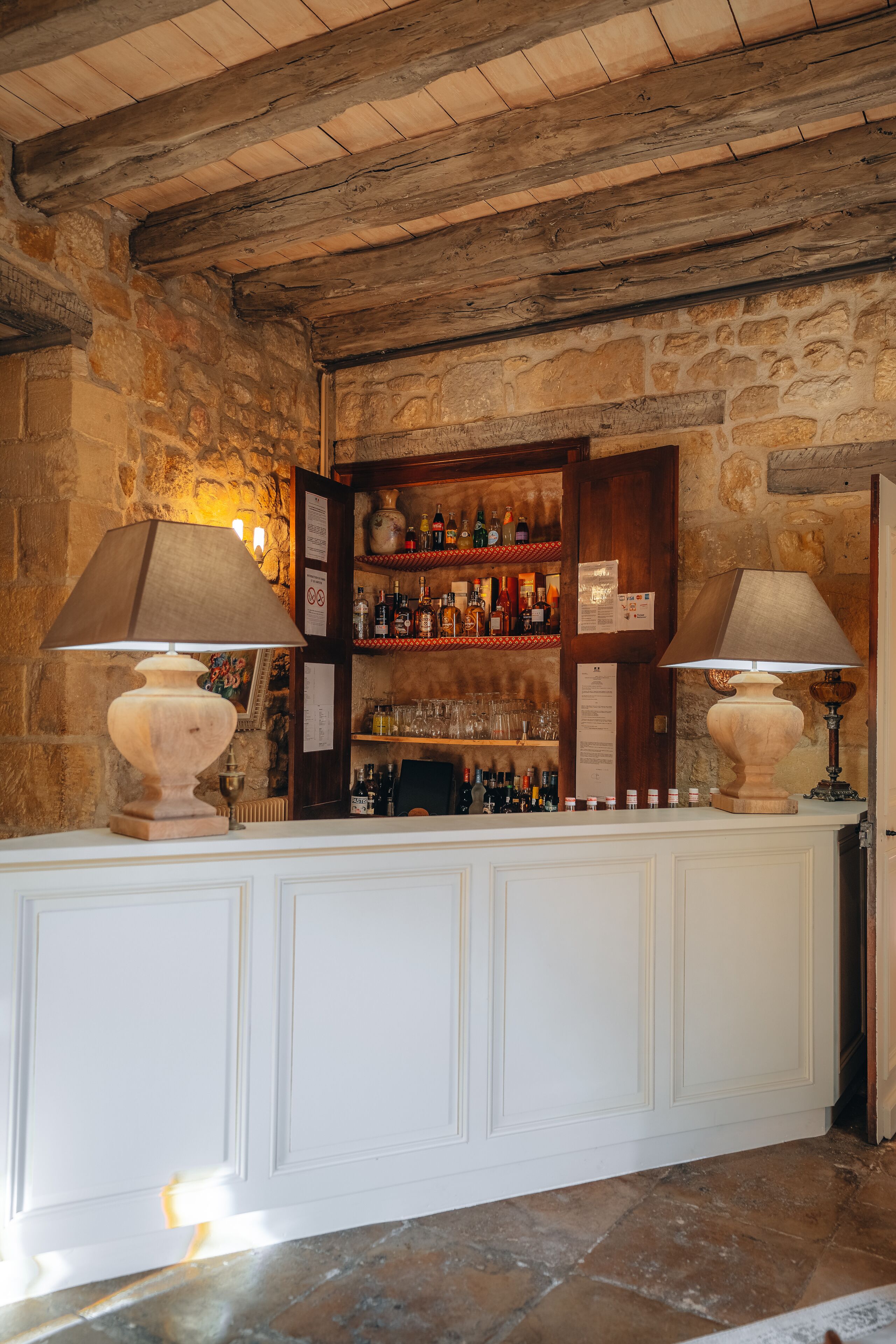 Eine Bar mit einer Steinsäule, Holzbalken an der Decke und einer weißen Theke mit zwei Lampen.