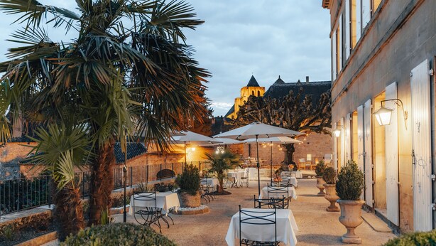 An outdoor dining area with tables and chairs, surrounded by palm trees and potted plants. - Hotel L'abbaye (Saint-Cyprien)