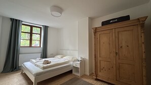 A bedroom with a bed, a wooden wardrobe, a window with curtains, and a radiator.
