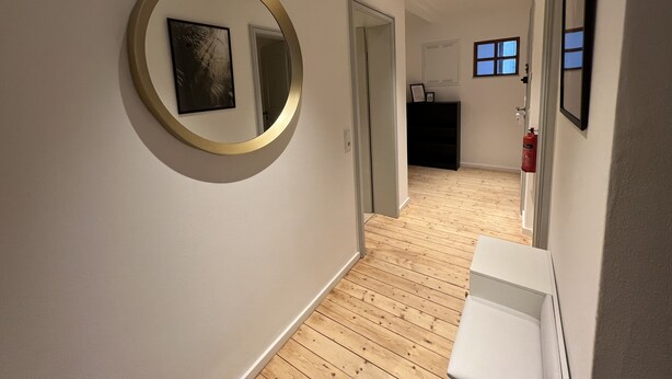 A hallway with a round mirror, a framed picture, a wooden floor, and a white wall.