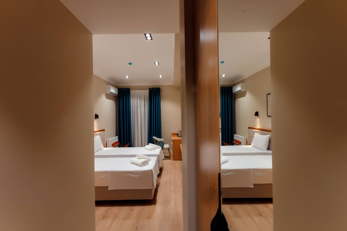 A hotel room with two beds, a wooden floor, and a mirror reflecting the room.