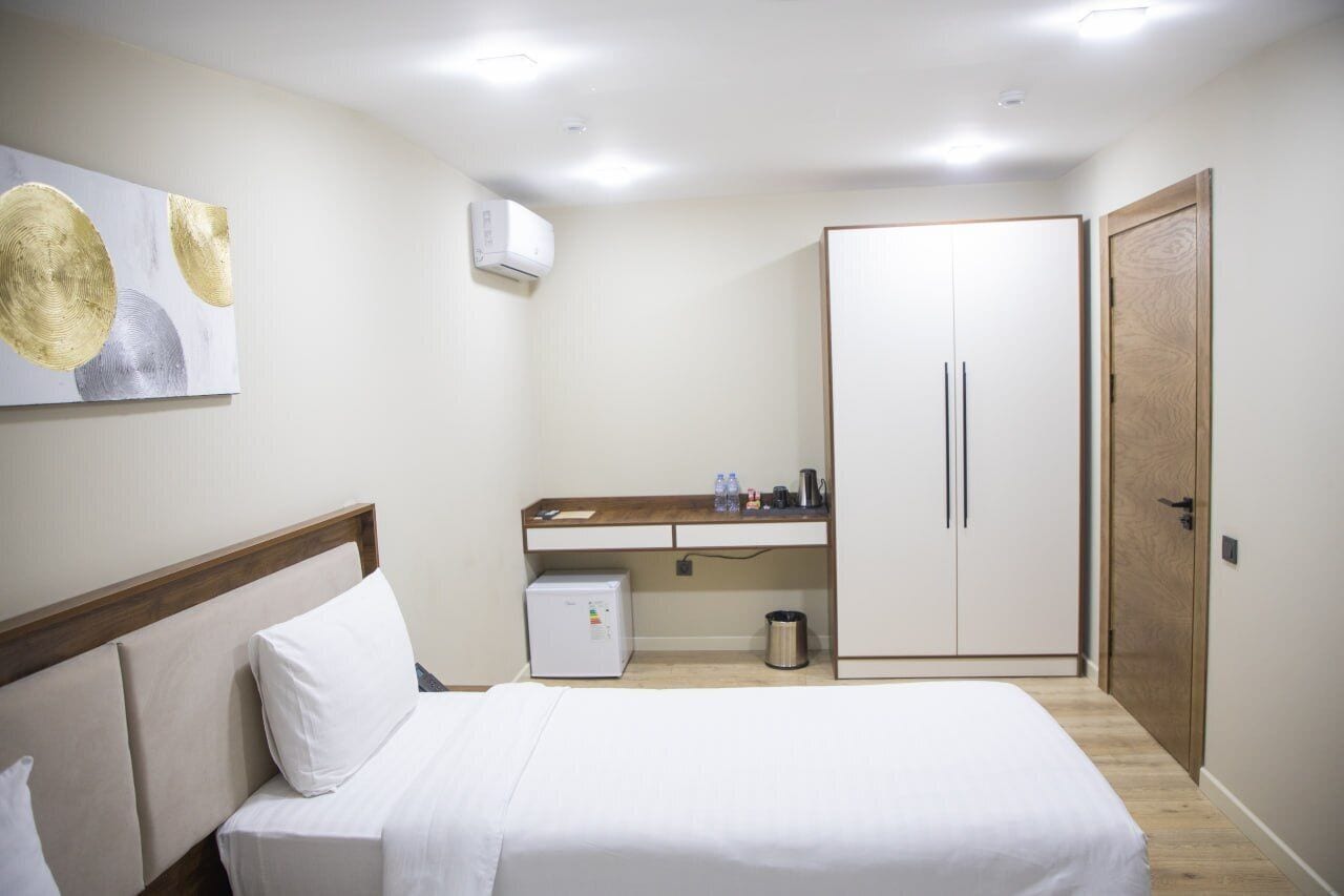 A hotel room with a bed, a desk, a wardrobe, and a wall-mounted air conditioner.