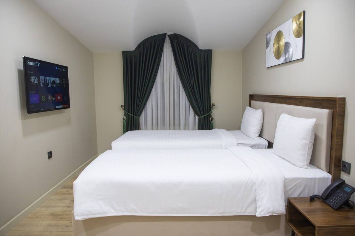A hotel room with two beds, a flat-screen TV, a telephone, and a painting on the wall.