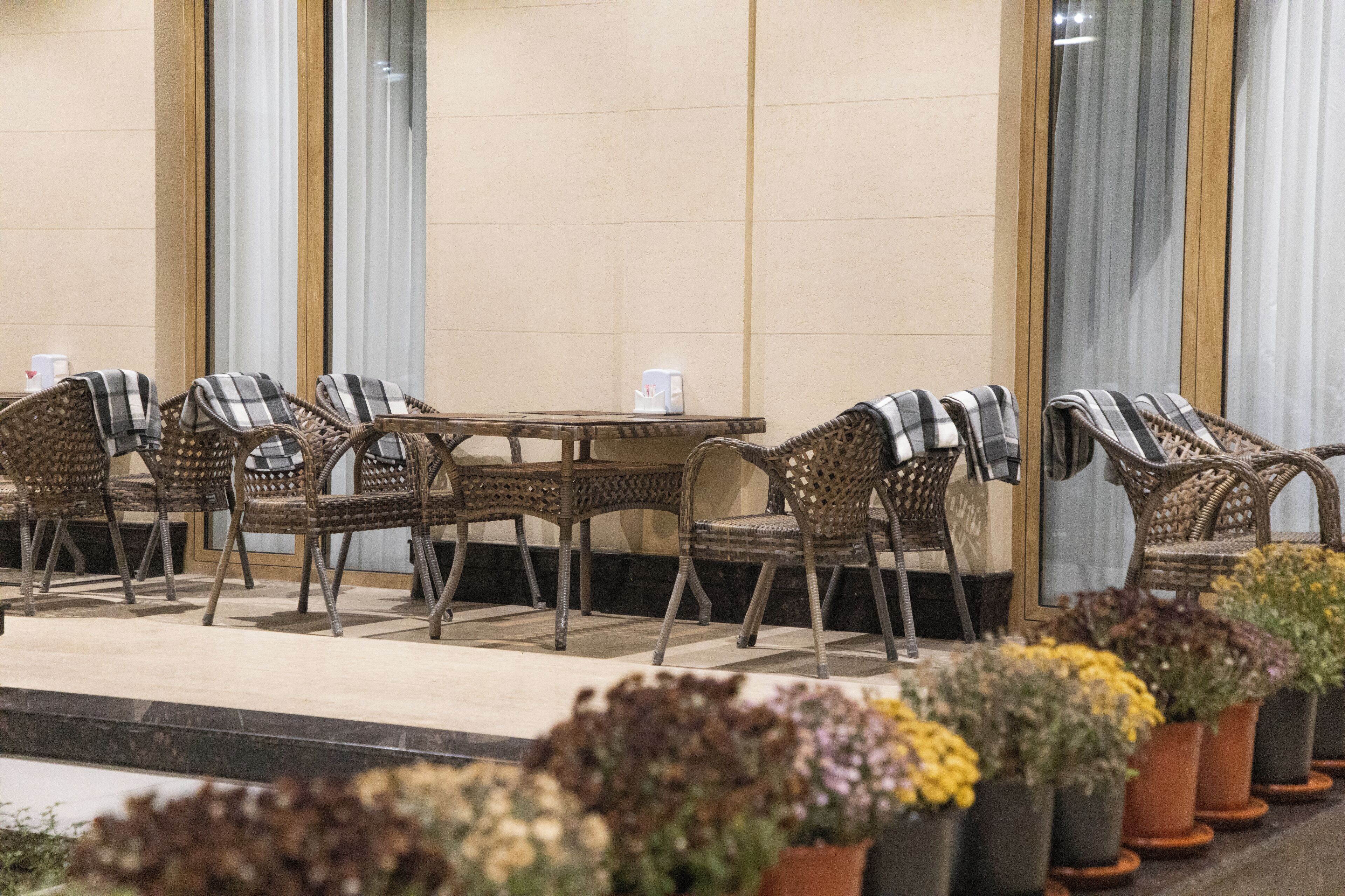 Wicker furniture with a table and chairs arranged on a terrace with potted plants.