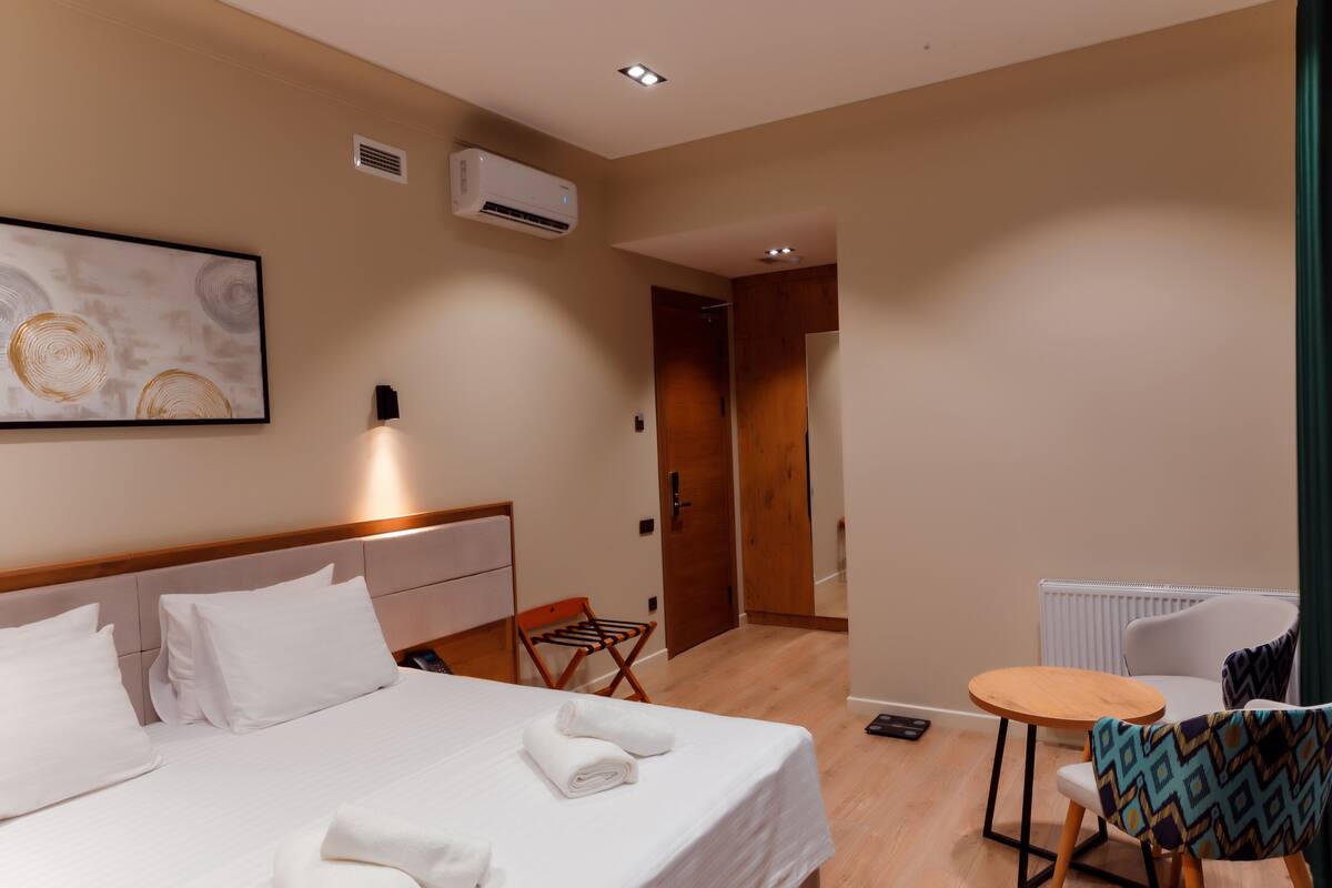 A hotel room with a bed, a chair, a small table, and a radiator.