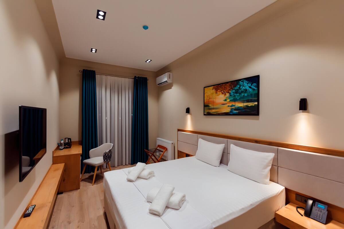 A hotel room with a large bed, a desk with a chair, a TV, and a painting on the wall.