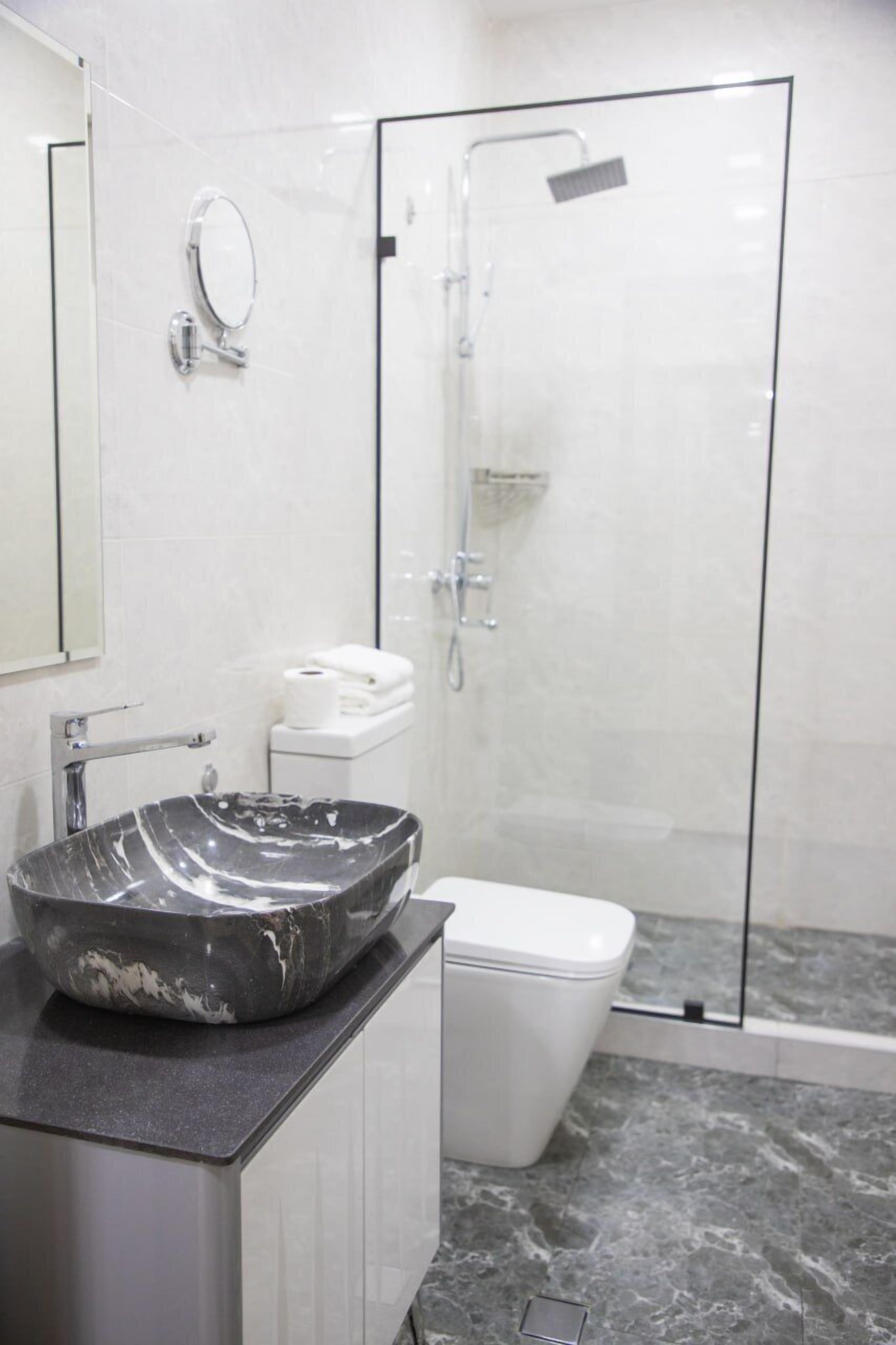 A modern bathroom with a marble sink, a toilet, and a glass-enclosed shower.