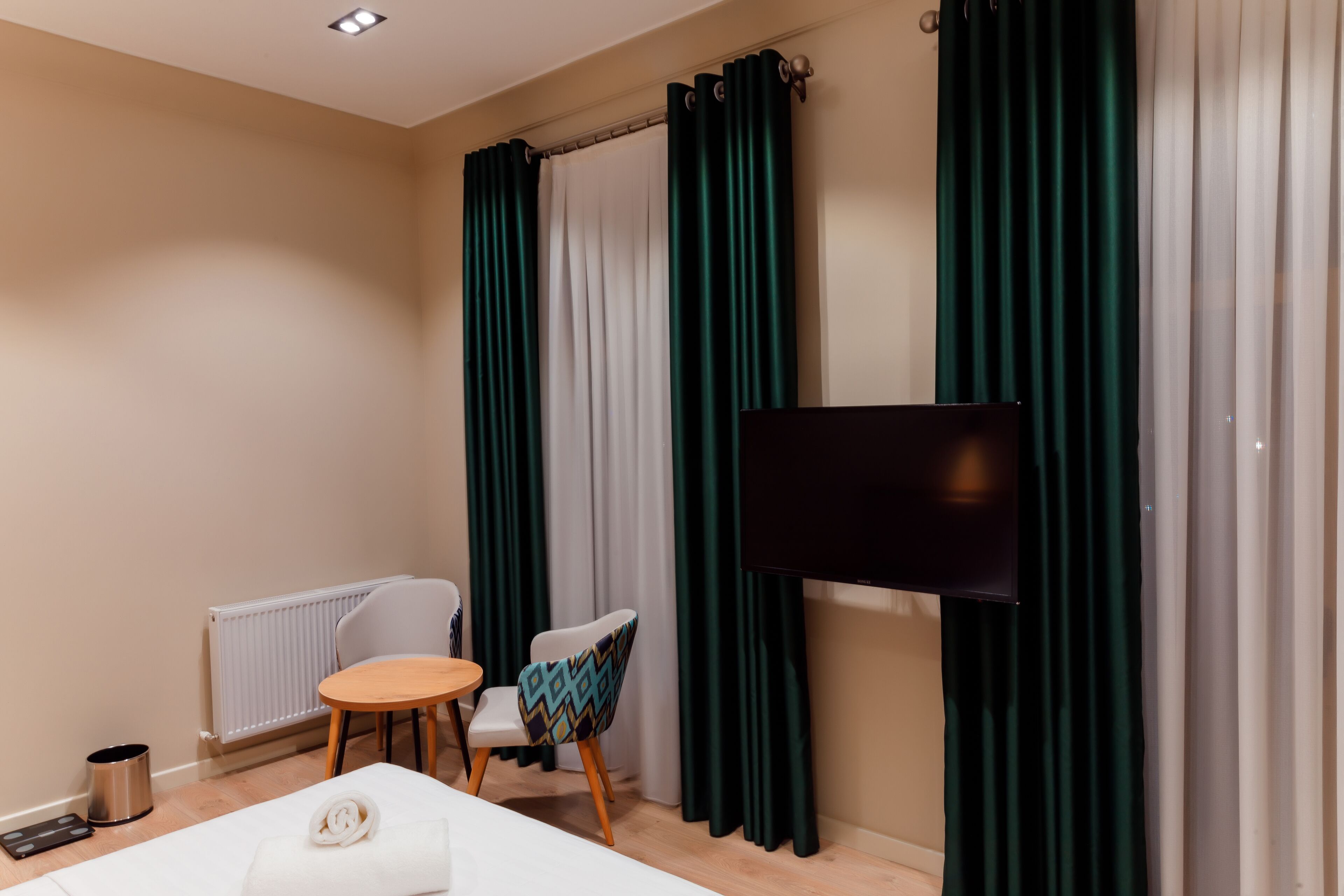 A hotel room with a bed, a small round table, a chair, a TV, and curtains.