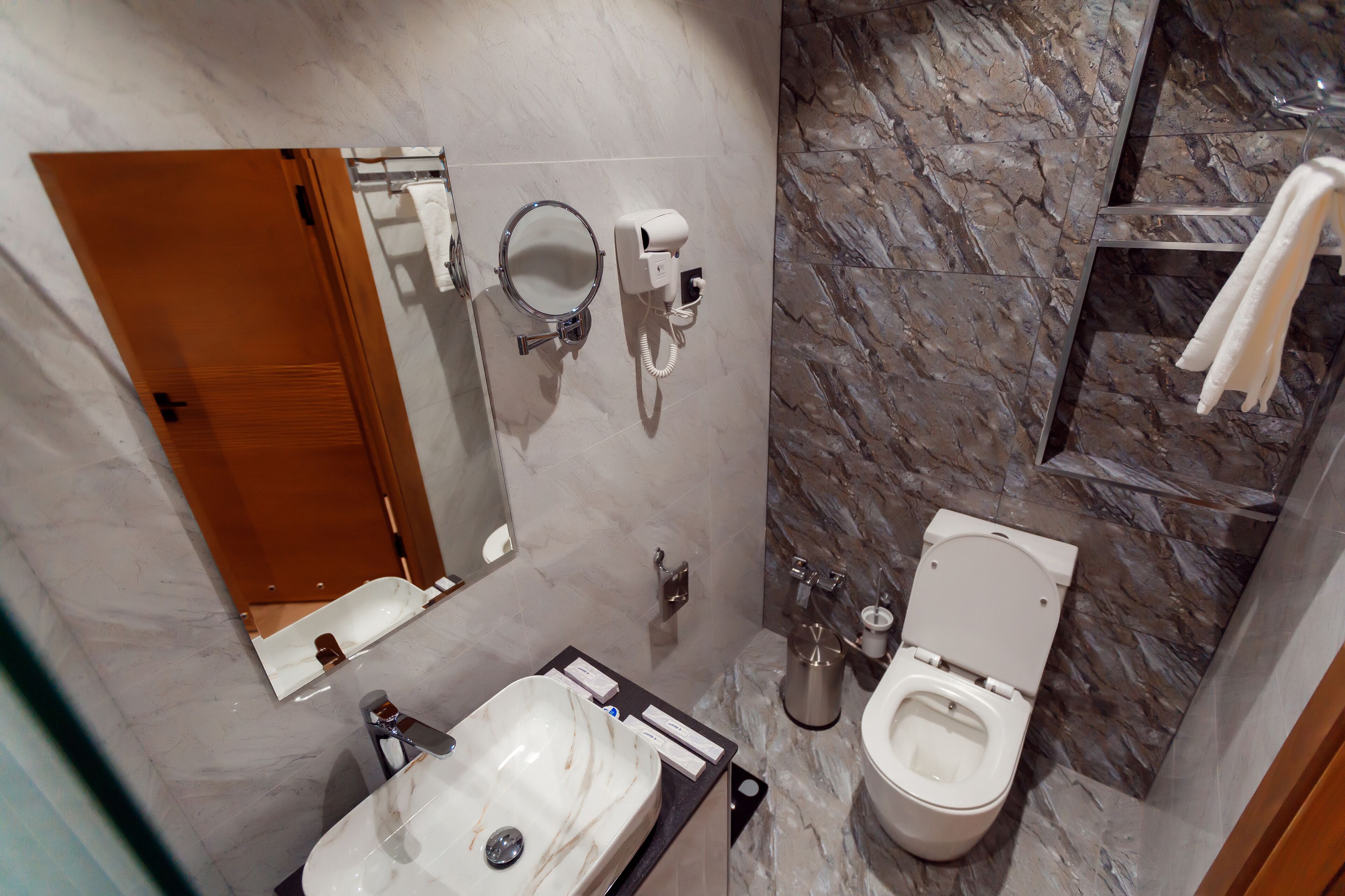 Un baño con lavamanos de mármol, inodoro, espejo y toallero.