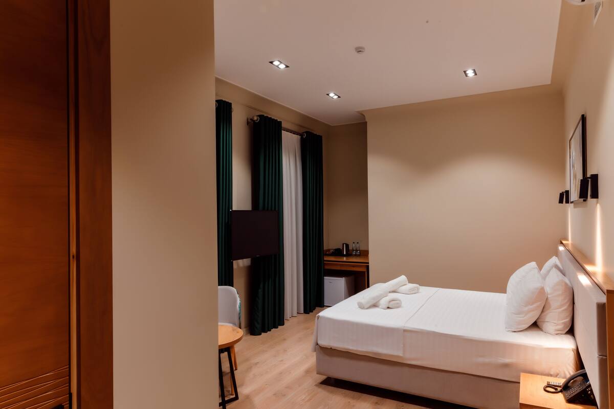 A hotel room with a bed, a desk, a chair, a TV, and a phone on the side table.