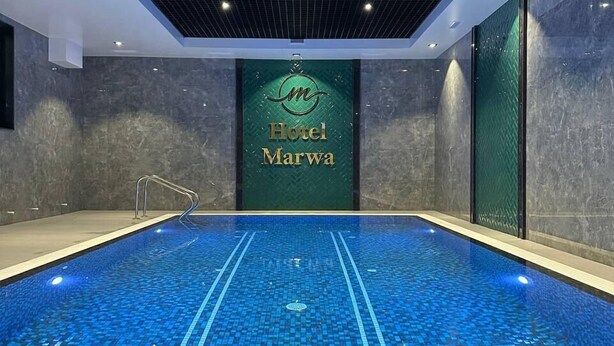 Piscina interior com chão em mosaico e placa com a inscrição "Hotel Marwa".
