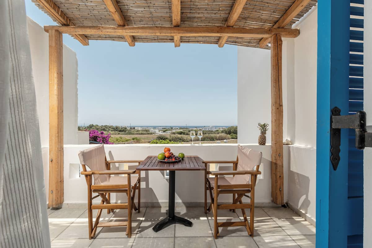 A covered outdoor seating area with a table and chairs, overlooking a scenic landscape.