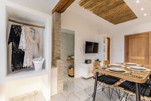 A dining area with a wooden table set for four, a television mounted on the wall, and a clothing rack with various garments. - Naxian Serenity Suites  (Naxos)