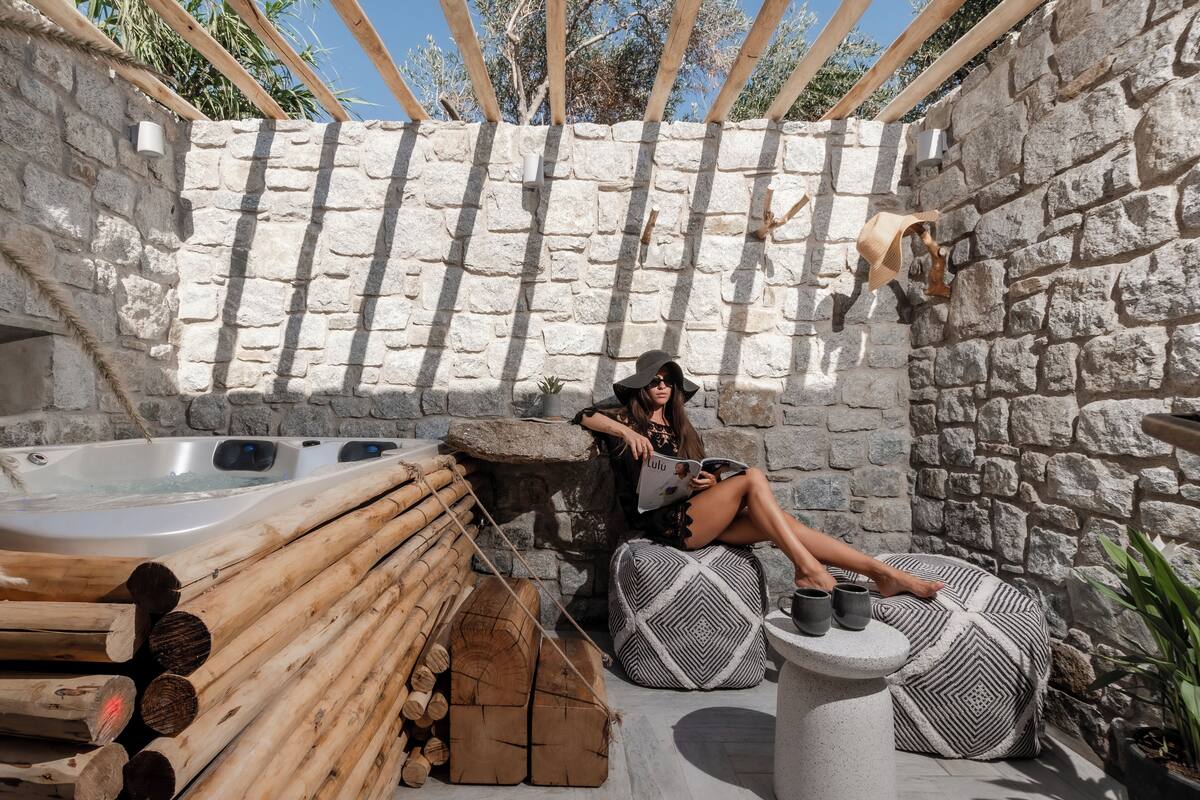A stone-walled outdoor seating area with a hot tub, wooden logs, and a patterned ottoman.