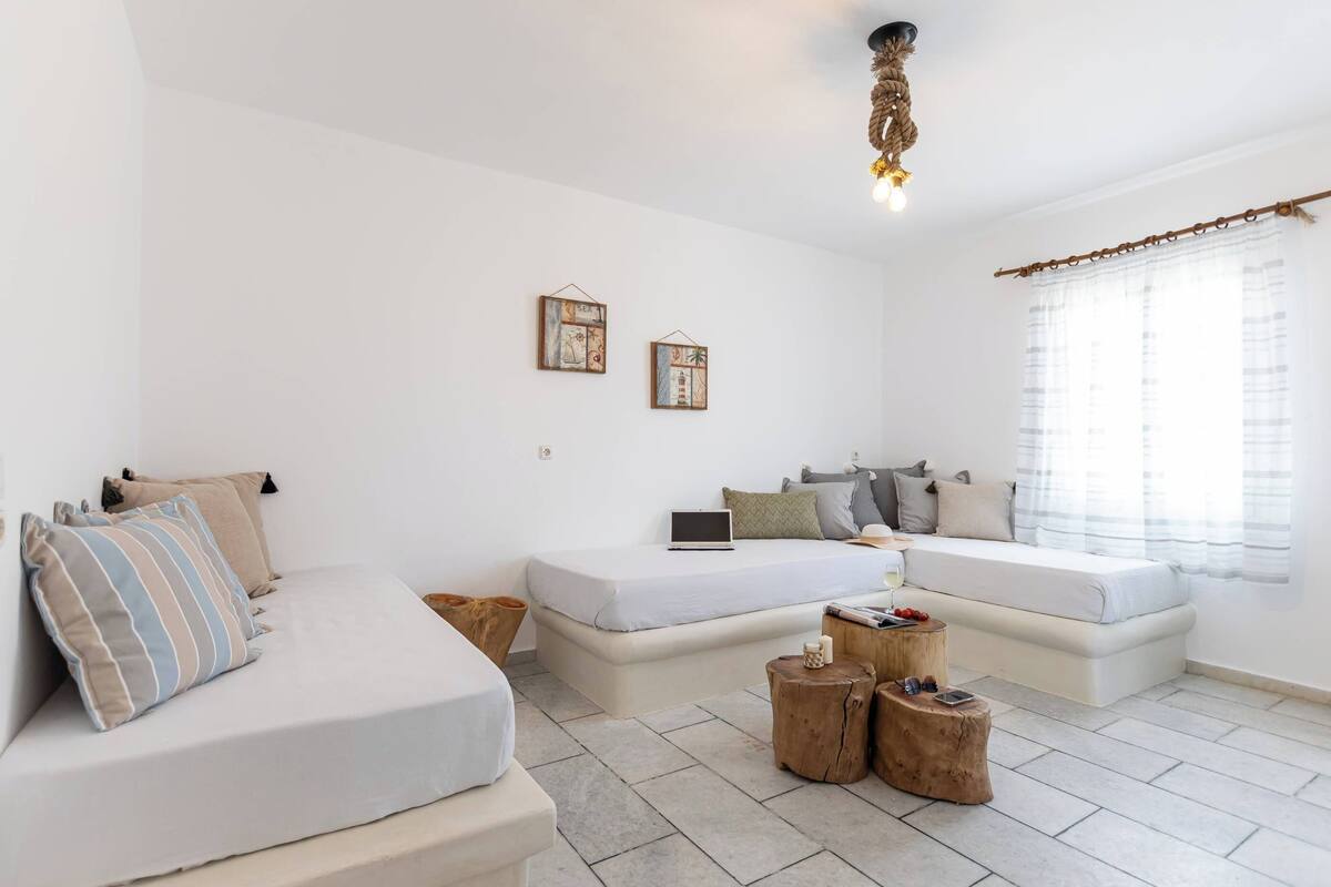 A modern, minimalist bedroom with two beds, a laptop on one bed, and a small wooden table with a cup and remote.