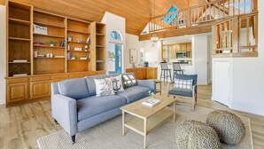 Amplia sala de estar con techo alto, vigas de madera, un sofá, una mesa de centro y vistas al área de la cocina y el comedor.