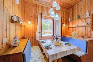 Interno di una baita in legno con un tavolo da pranzo apparecchiato per quattro persone, una panca e una finestra con tende.