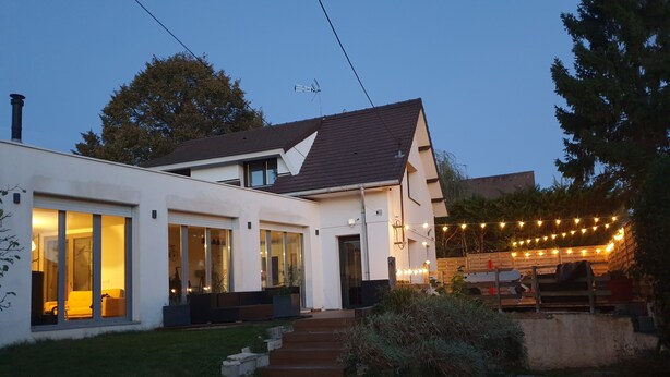 A modern house with large windows, a visible staircase, and outdoor string lights.
