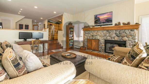 A spacious living room with a stone fireplace, comfortable seating, a television, and a kitchen area in the background. - An unforgettable escape to Lake Tahoe (MC250) (Incline Village)