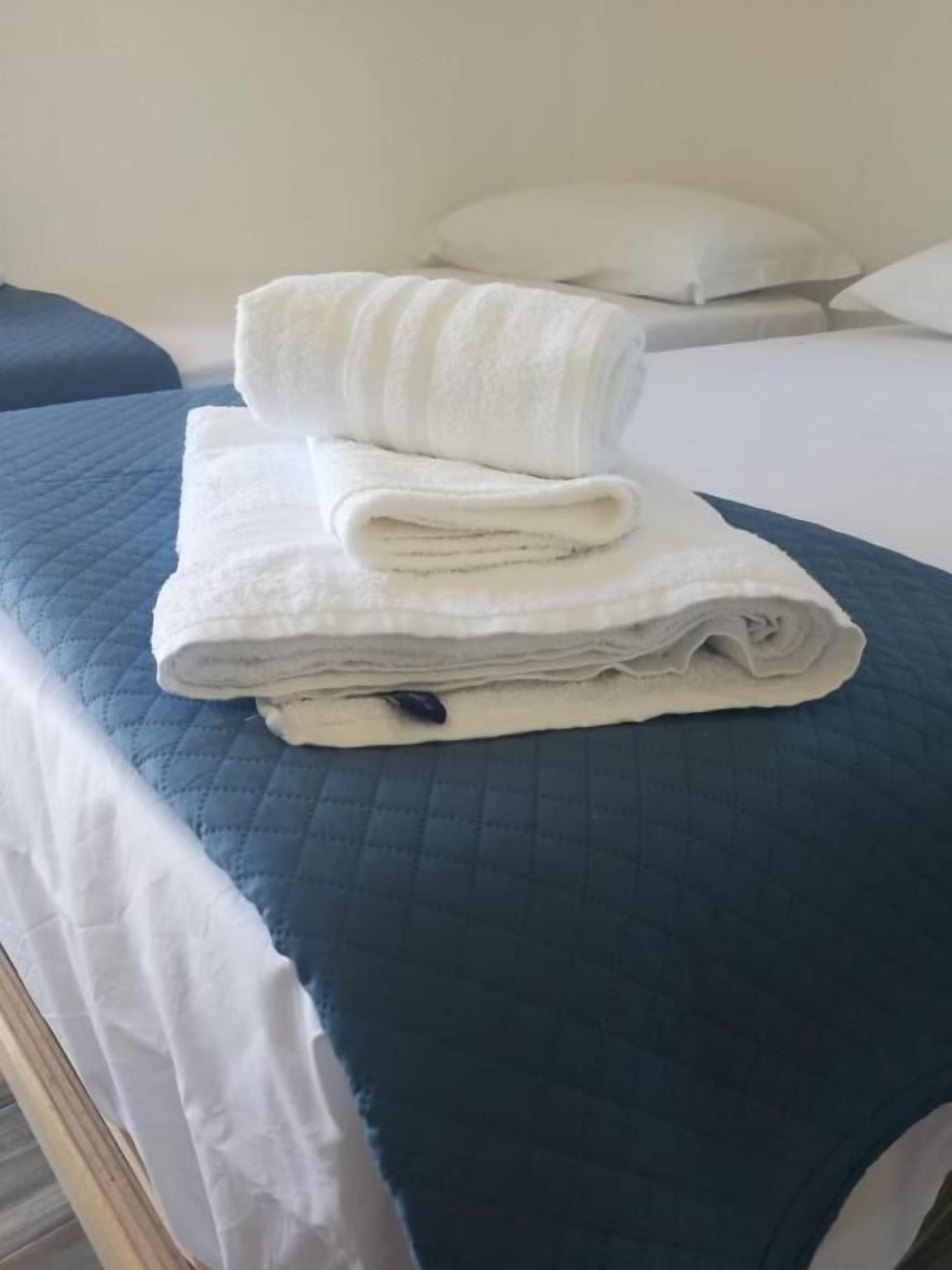 Una cama bien hecha con un edredón azul acolchado y dos toallas blancas dobladas encima.