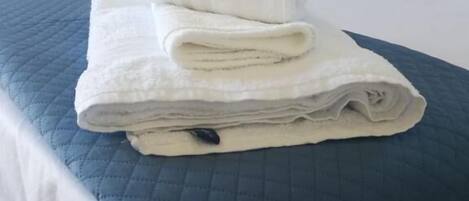 A neatly made bed with a blue quilted bedspread and two folded white towels on top.