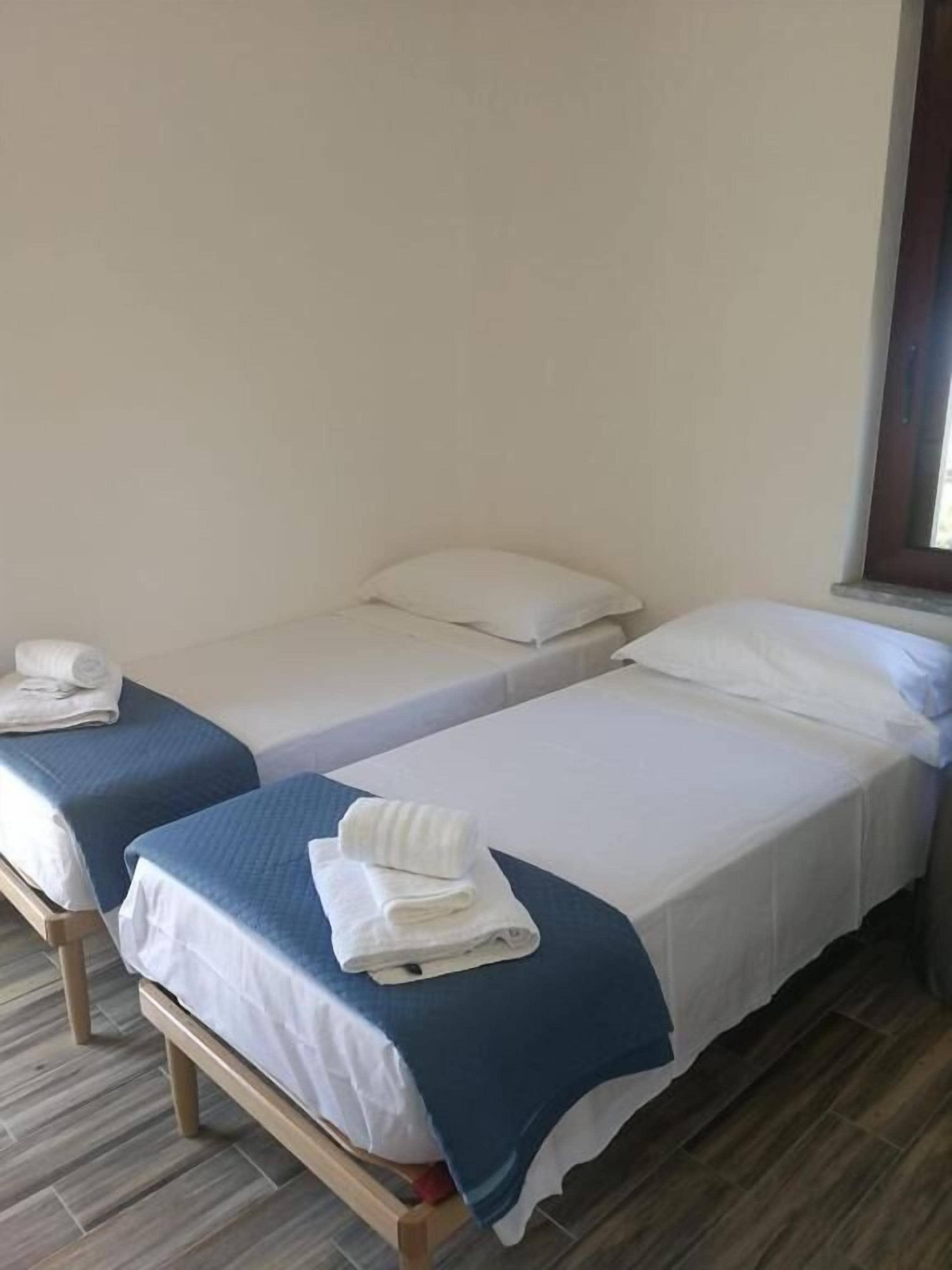 Una habitación con dos camas individuales, cada una con una manta azul y almohadas blancas, y suelo de madera.