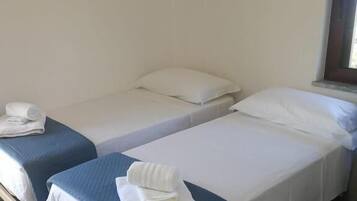 Una habitación con dos camas individuales, cada una con una manta azul y almohadas blancas, y suelo de madera.