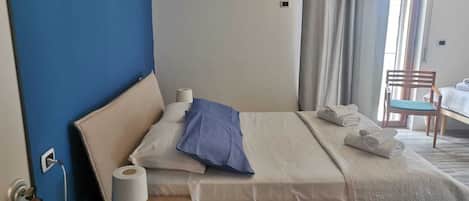 A hotel room with a bed, a wooden nightstand, a chair, and a window with curtains.