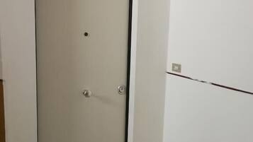 Puerta cerrada con manija y cerradura, suelo de mármol y pared blanca con un enchufe a la vista.