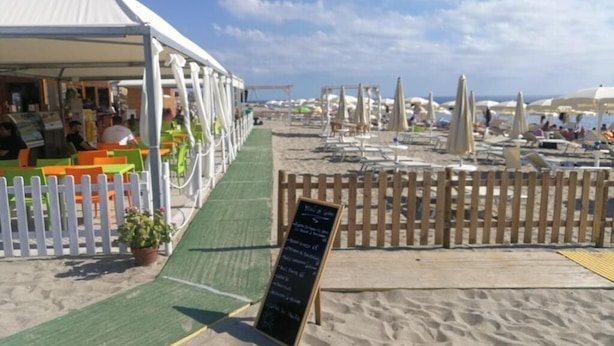 A beachside restaurant with outdoor seating, a white fence, and a green pathway leading to the beach. - b&b Crispino (Belvedere Marittimo)