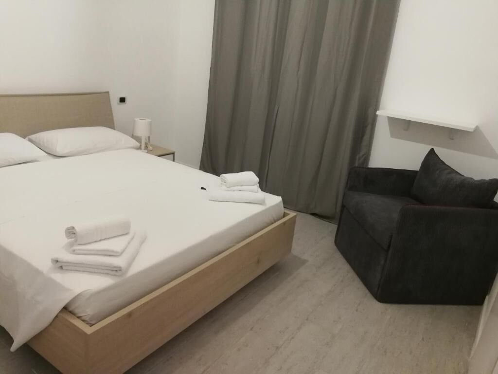 A neatly made bed with white linens and towels, a wooden headboard, a dark armchair, and a small bedside table with a lamp.