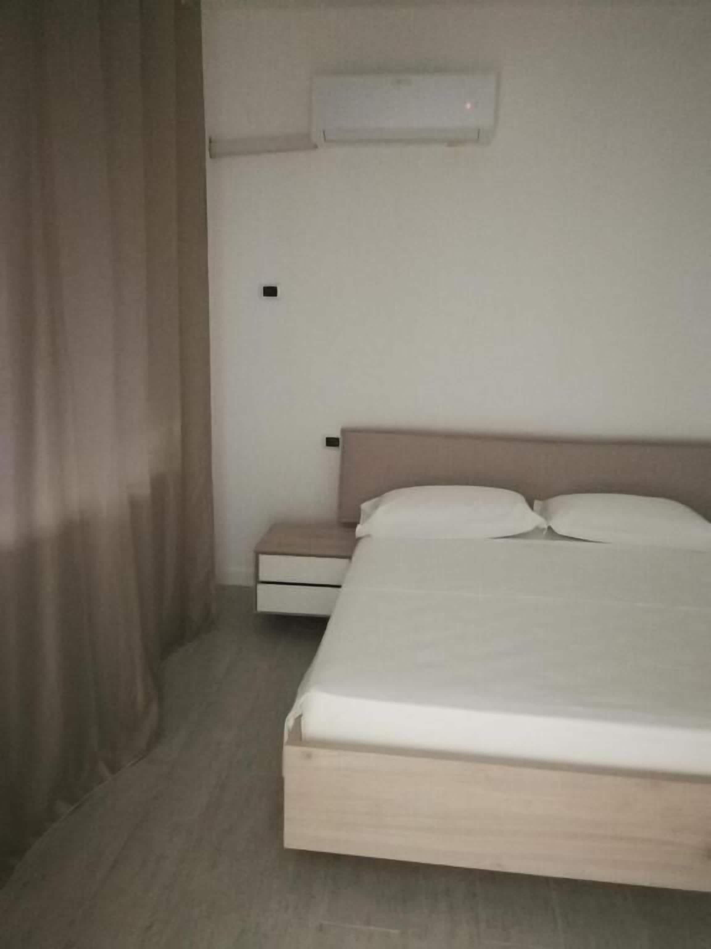 Una habitación de hotel con una cama, una mesita de noche, un cajón y un equipo de aire acondicionado en la pared.