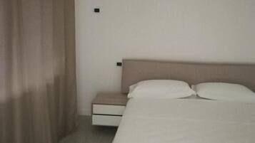 Une chambre d’hôtel avec un lit, une table de chevet, un tiroir et un appareil de climatisation fixé au mur.